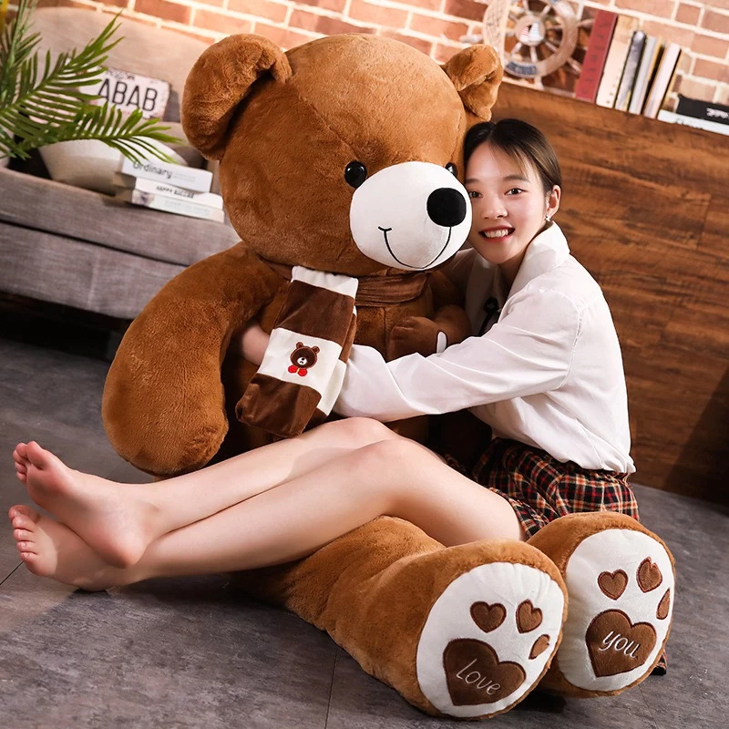 דובי בגודל 2 מטר בצבע חום, עם צעיף בצבע חום לבן על הצוואר, ואישה שיושבת על הדובי.